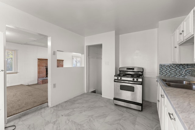 kitchen featuring white cabinetry, sink, a brick fireplace, stainless steel gas range oven, and decorative backsplash