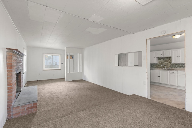 unfurnished living room featuring light carpet, sink, and a brick fireplace