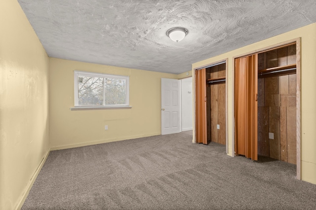 unfurnished bedroom featuring carpet floors, two closets, and a textured ceiling