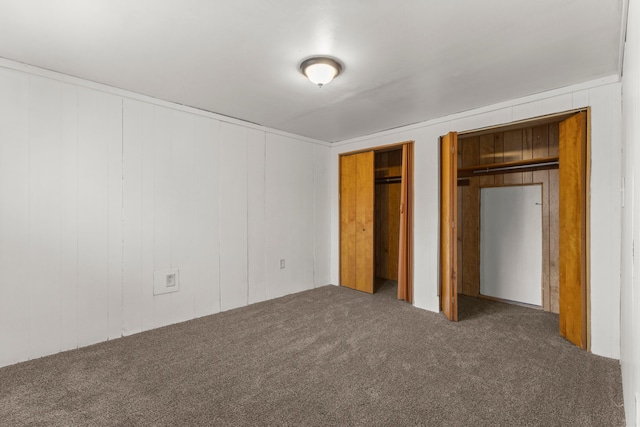 unfurnished bedroom featuring multiple closets, wood walls, and dark colored carpet