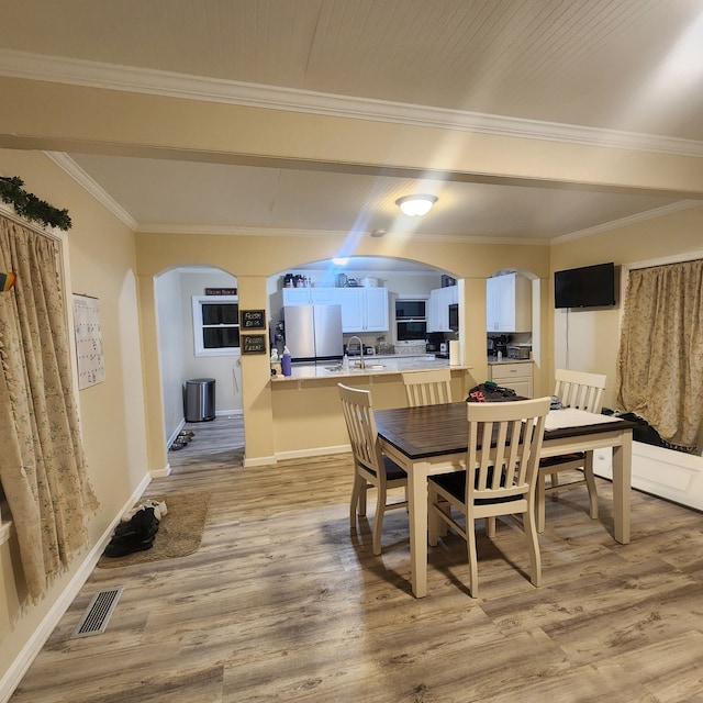 dining space with light hardwood / wood-style floors, crown molding, and sink