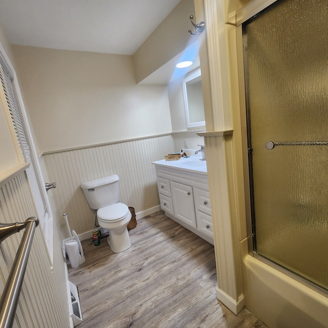 8789 Fowlerville Rd, Fowlerville, MI 48836 - bathroom featuring wood finished floors, toilet, vanity, wainscoting, and shower / bath combination with glass door