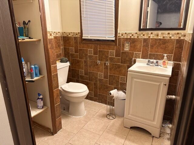 bathroom featuring tile patterned flooring, vanity, toilet, and tile walls