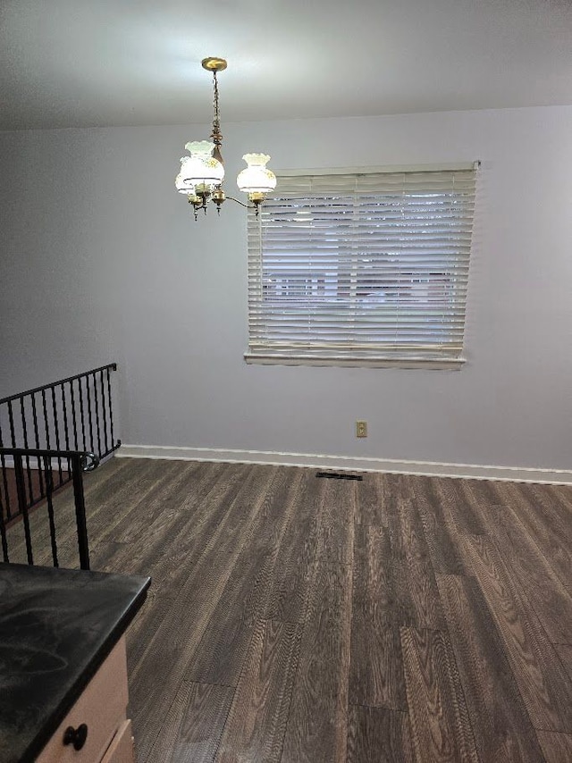 spare room featuring dark hardwood / wood-style flooring and an inviting chandelier