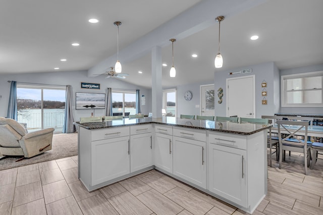 kitchen with ceiling fan, white cabinetry, a kitchen island, decorative light fixtures, and dark stone counters