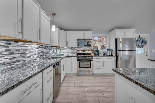 kitchen with white cabinetry, appliances with stainless steel finishes, sink, and dark stone countertops