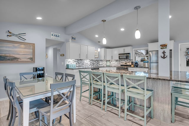 kitchen with dark stone countertops, vaulted ceiling with beams, white cabinetry, stainless steel appliances, and decorative light fixtures