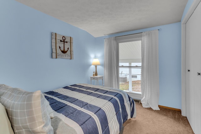 bedroom with light colored carpet, vaulted ceiling, a closet, and a textured ceiling