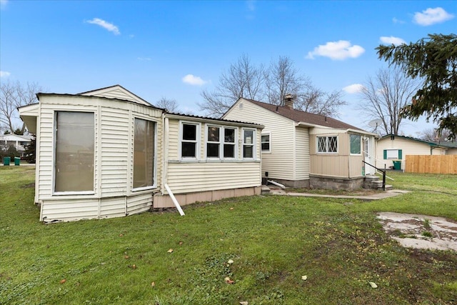 back of house featuring entry steps, a lawn, and fence