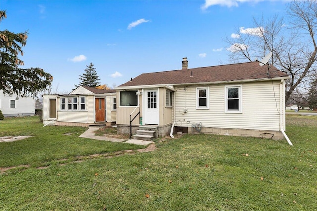 back of house featuring entry steps, a yard, a chimney, and roof with shingles