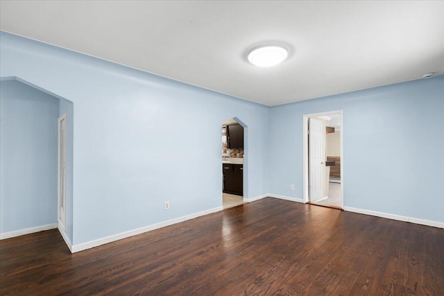 spare room featuring baseboards, arched walkways, and wood finished floors