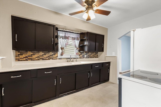 kitchen with electric range, arched walkways, light countertops, open shelves, and a sink