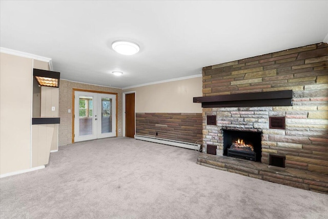 unfurnished living room featuring french doors, crown molding, baseboard heating, carpet flooring, and a stone fireplace