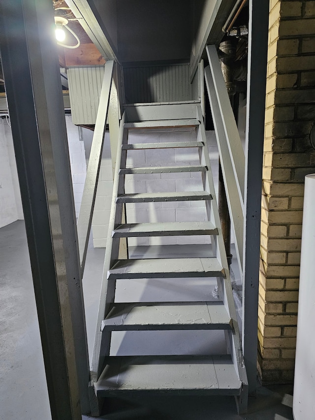 staircase featuring concrete flooring and brick wall