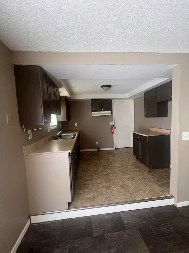 kitchen with dark brown cabinetry, sink, and a textured ceiling