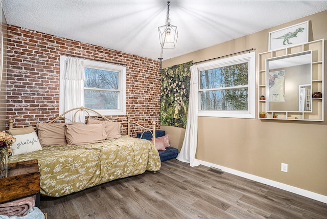 bedroom with visible vents, a textured ceiling, brick wall, wood finished floors, and baseboards