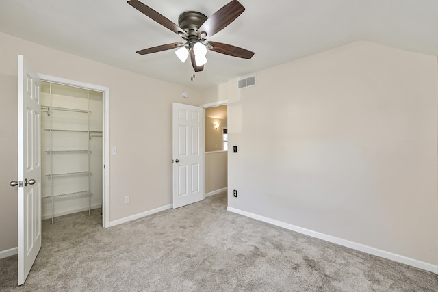 unfurnished bedroom featuring a walk in closet, ceiling fan, a closet, and light carpet