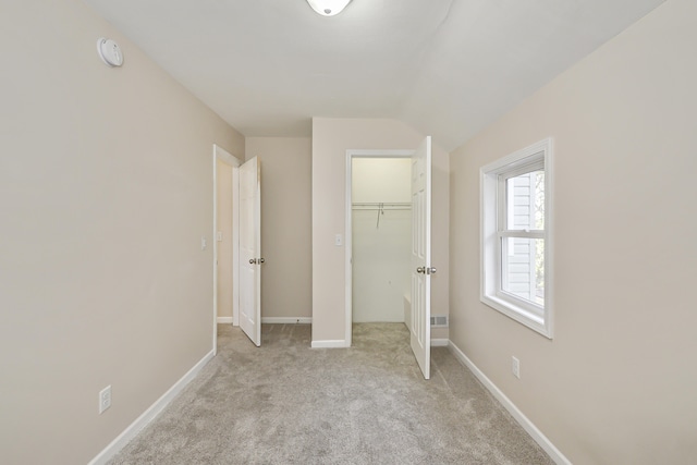 unfurnished bedroom with a closet, a walk in closet, light carpet, and vaulted ceiling