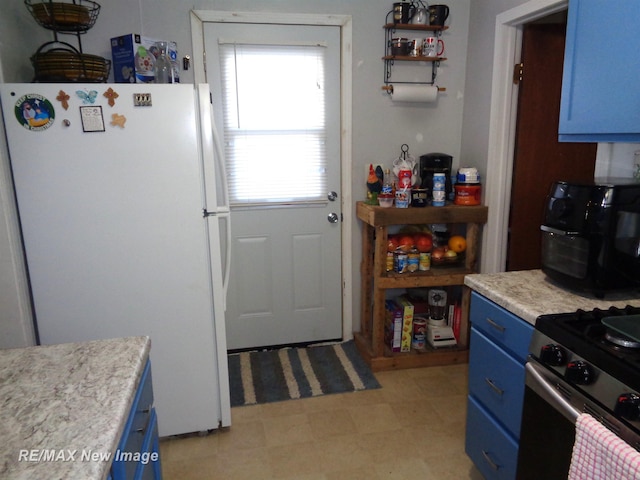 kitchen with white fridge, blue cabinetry, and stainless steel gas range