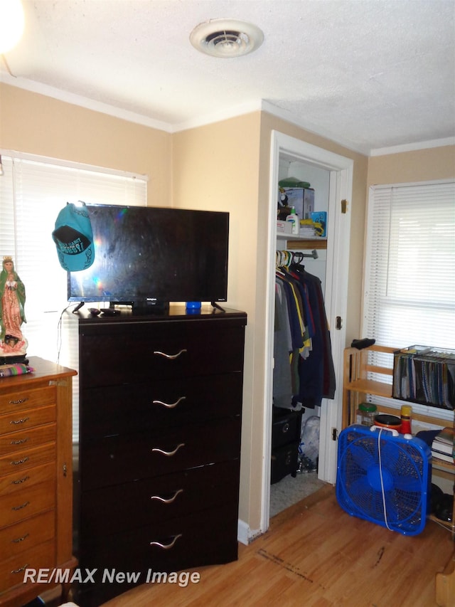 bedroom featuring a textured ceiling, light hardwood / wood-style floors, a closet, and ornamental molding