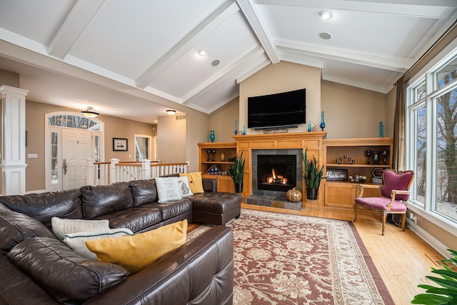 living area with vaulted ceiling with beams, decorative columns, a lit fireplace, and hardwood / wood-style floors