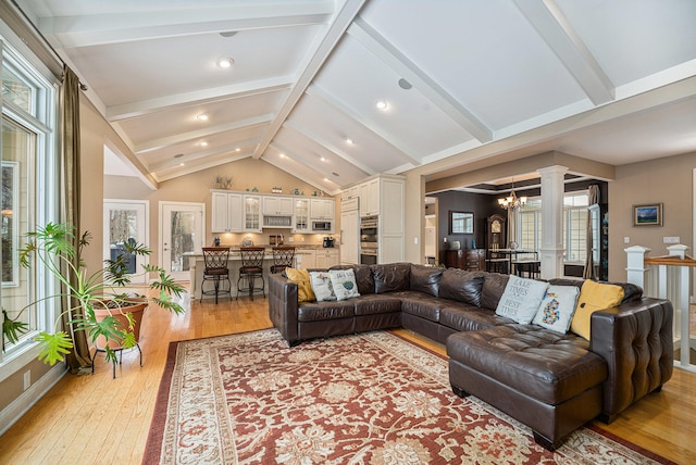 living area featuring vaulted ceiling with beams, baseboards, a chandelier, light wood-type flooring, and ornate columns