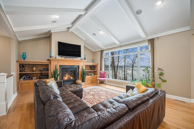 living area with visible vents, light wood-style flooring, lofted ceiling with beams, and a glass covered fireplace