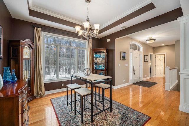 dining room with crown molding, baseboards, a tray ceiling, light wood-style flooring, and an inviting chandelier