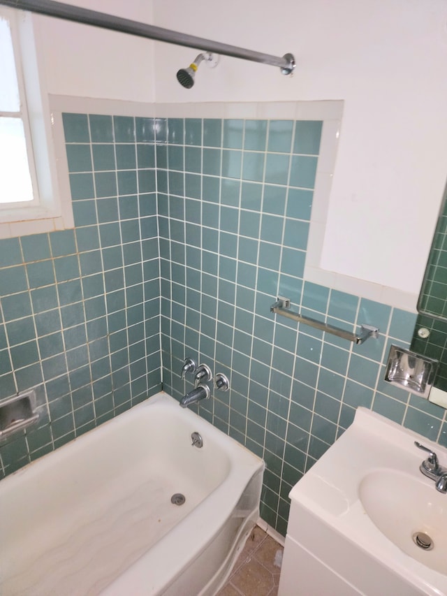 bathroom with tile patterned flooring, tiled shower / bath combo, tile walls, and sink