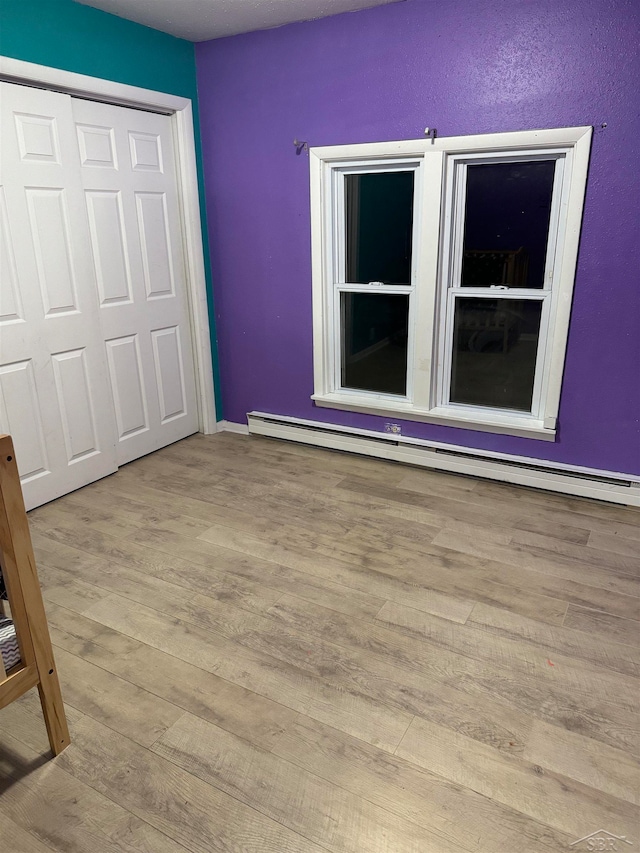 unfurnished bedroom with light hardwood / wood-style floors, a closet, and a baseboard heating unit