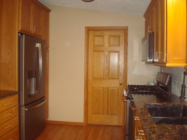 kitchen with dark stone countertops, stainless steel appliances, a textured ceiling, and light wood-type flooring