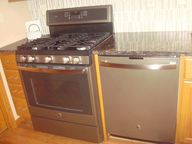 details with light hardwood / wood-style floors, dark stone countertops, and stainless steel appliances