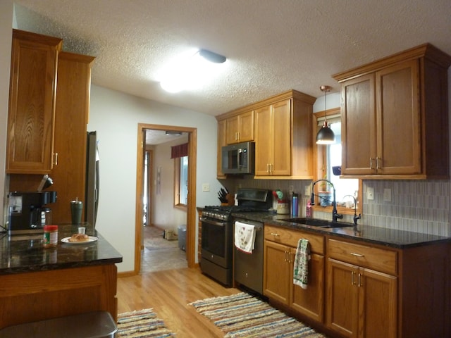 kitchen with appliances with stainless steel finishes, backsplash, sink, decorative light fixtures, and light hardwood / wood-style floors