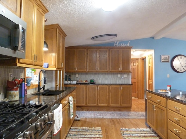 kitchen featuring sink, vaulted ceiling with beams, dark stone countertops, light wood-type flooring, and tasteful backsplash