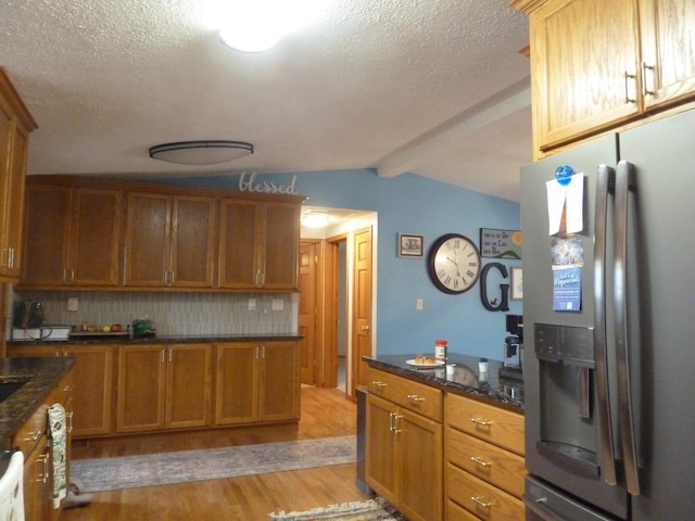 kitchen with decorative backsplash, stainless steel fridge, dark stone countertops, vaulted ceiling with beams, and light hardwood / wood-style floors