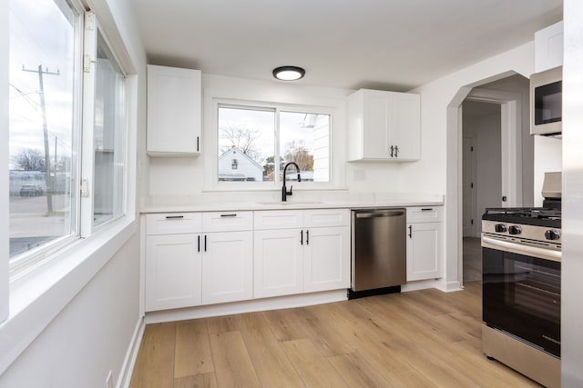 kitchen with appliances with stainless steel finishes, light hardwood / wood-style floors, white cabinetry, and sink