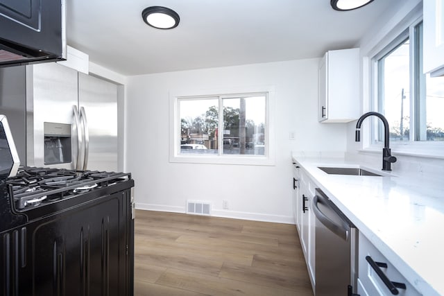 kitchen with light stone countertops, appliances with stainless steel finishes, sink, light hardwood / wood-style flooring, and white cabinetry