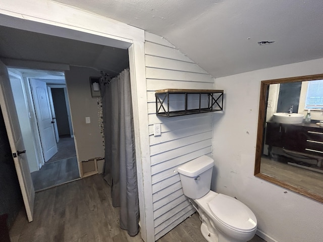 bathroom featuring vanity, wood walls, vaulted ceiling, toilet, and wood-type flooring