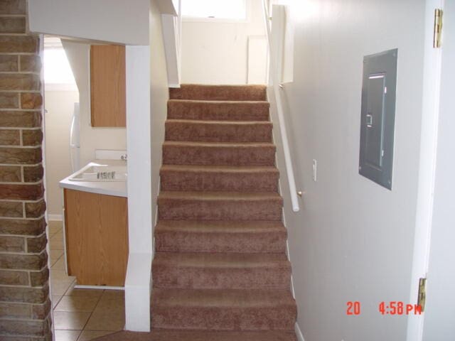 stairway with tile patterned floors, sink, and electric panel