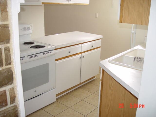 kitchen featuring white cabinets, sink, light tile patterned flooring, and electric stove