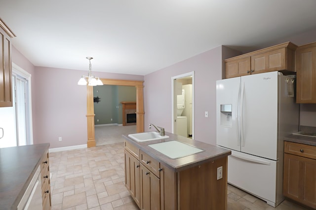 kitchen featuring white fridge with ice dispenser, sink, a notable chandelier, pendant lighting, and a center island with sink