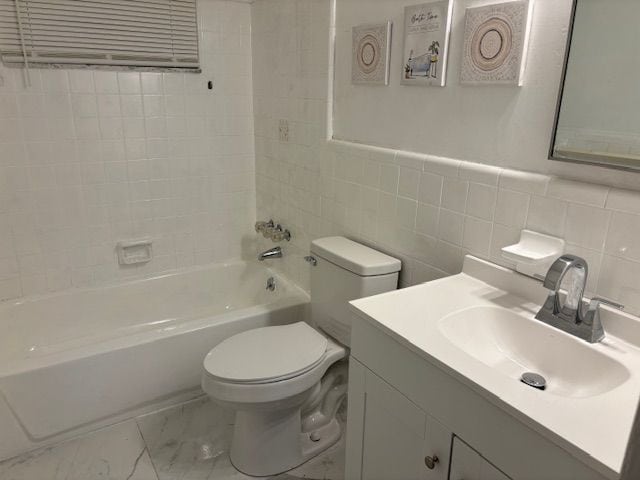 full bathroom with tiled shower / bath combo, toilet, tile walls, and vanity