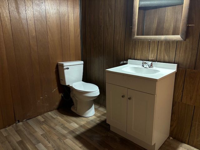 bathroom featuring hardwood / wood-style floors, vanity, wood walls, and toilet