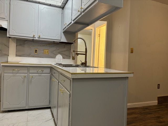 kitchen with backsplash, sink, gray cabinets, light wood-type flooring, and kitchen peninsula