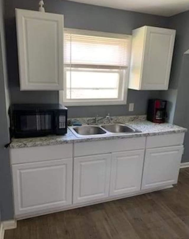 kitchen with white cabinets, dark hardwood / wood-style flooring, light stone countertops, and sink