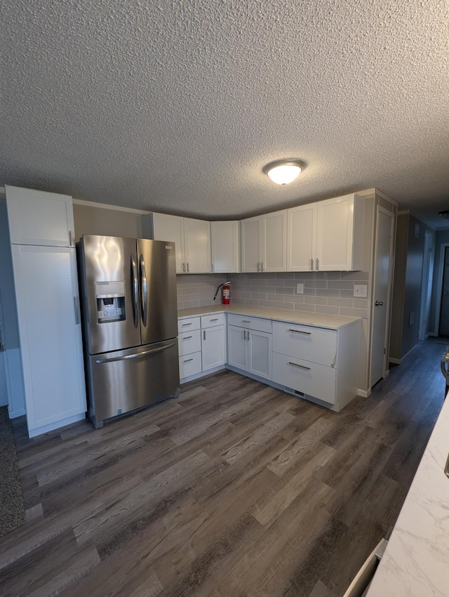 kitchen featuring white cabinetry, dark wood-type flooring, backsplash, stainless steel fridge, and a textured ceiling