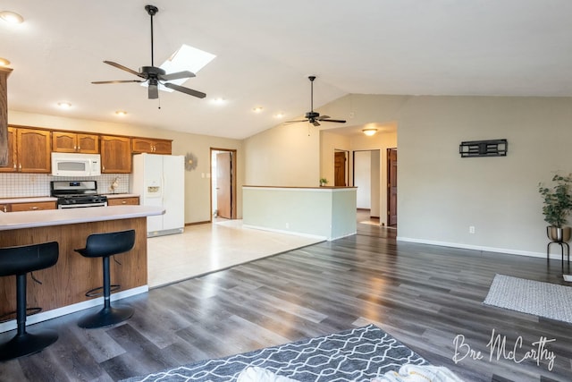 kitchen with ceiling fan, tasteful backsplash, dark hardwood / wood-style floors, white appliances, and vaulted ceiling with skylight