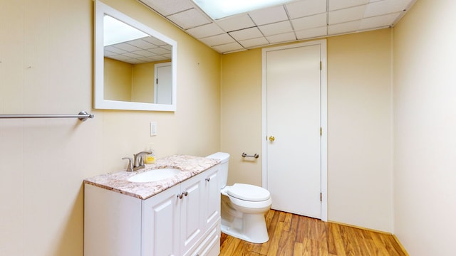 bathroom featuring wood-type flooring, vanity, toilet, and a drop ceiling