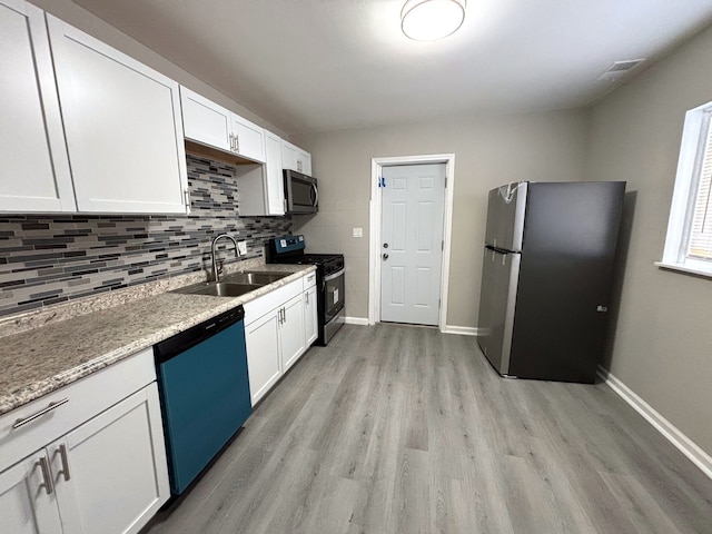 kitchen featuring white cabinetry, sink, light stone counters, light hardwood / wood-style flooring, and appliances with stainless steel finishes