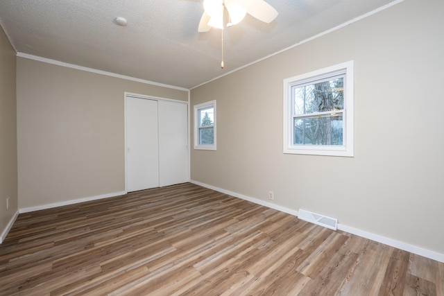 unfurnished bedroom featuring ceiling fan, hardwood / wood-style floors, a textured ceiling, a closet, and ornamental molding